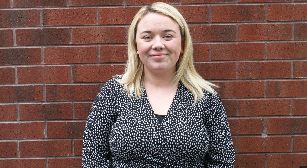 Woman with blonde hair and white spotted top pictured in front of a brick wall.